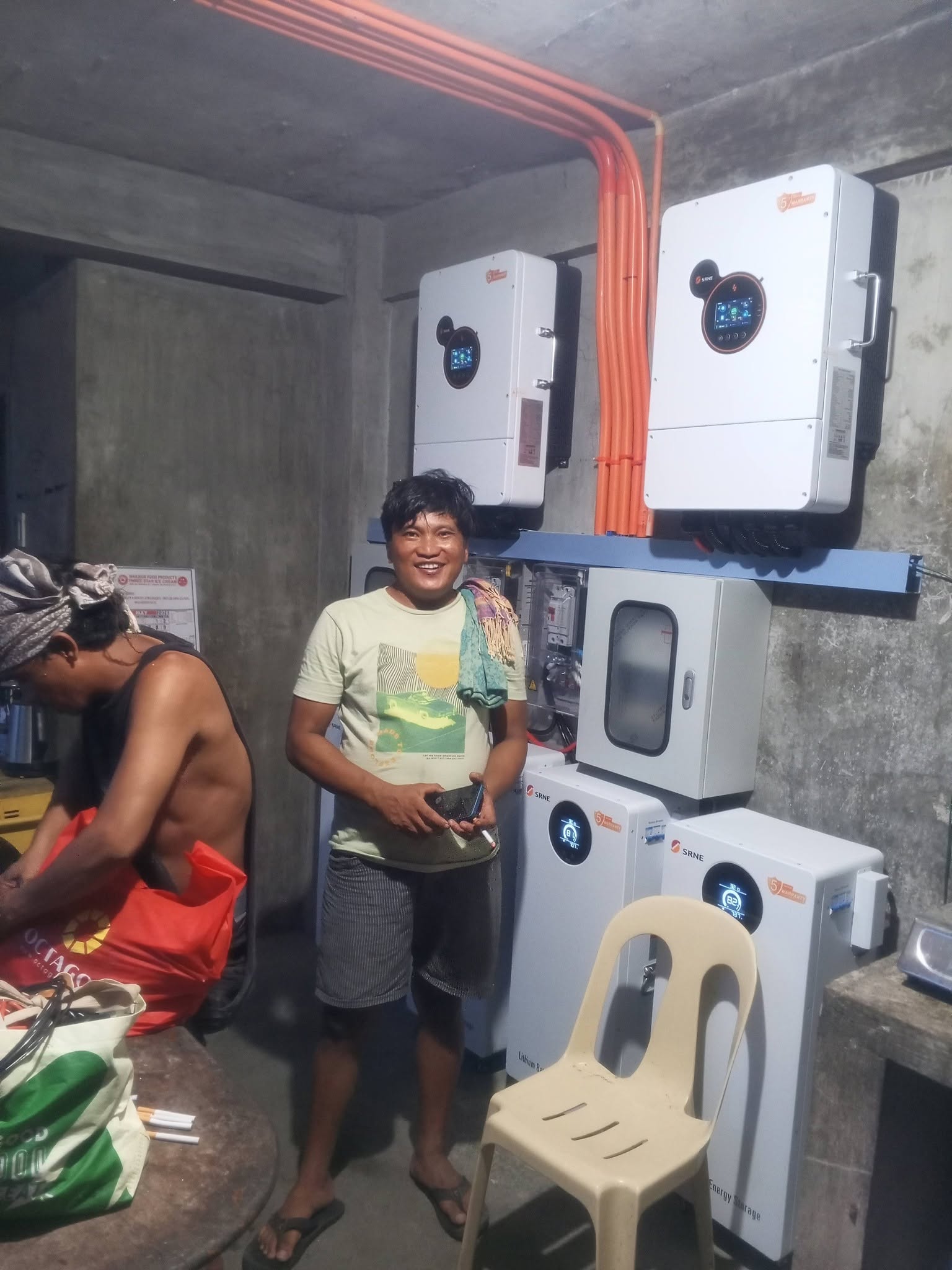 An installer beside a completed hybrid inverter and battery bank